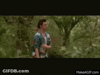 A Man In A White Tank Top Is Walking Through A Lush Green Forest GIF