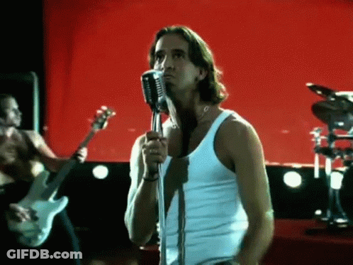 A Man In A White Tank Top Singing Into A Microphone GIF