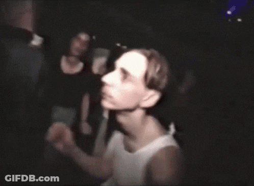 A Man In A White Tank Top Stands In Front Of A Group Of People GIF