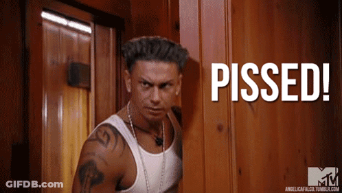 A Man In A White Tank Top Stands In Front Of A Wooden Door With The Words Pissed Written On It GIF