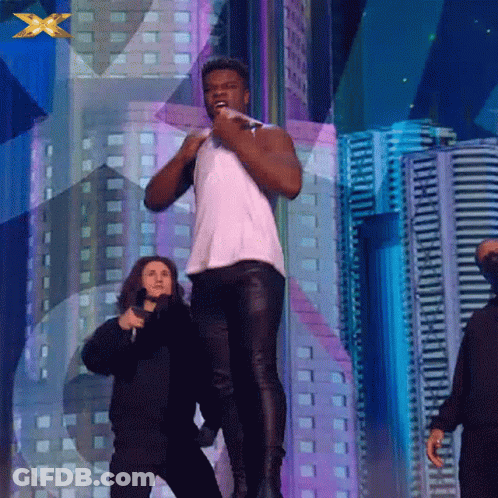 A Man In A White Tank Top Stands On A Stage With A Microphone In His Hand GIF