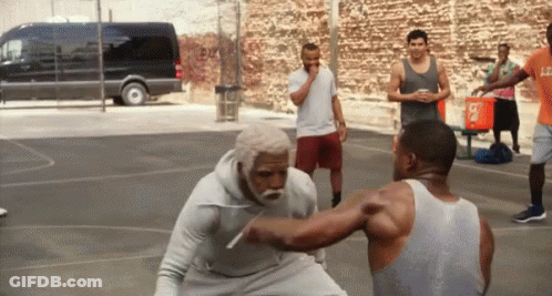 A Man In A White Tank Top With The Letter L On It Is Fighting Another Man On A Basketball Court GIF