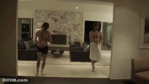 A Man In A White Towel Is Walking In A Living Room GIF
