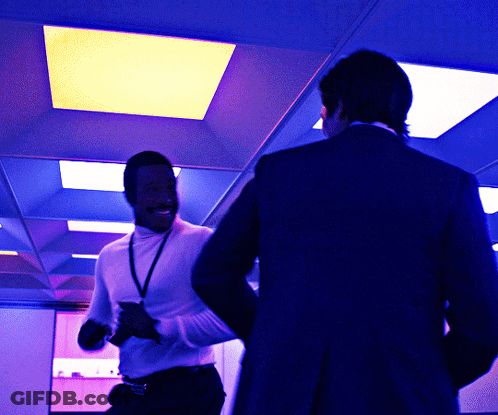 A Man In A White Turtleneck Is Standing Next To Another Man In A Black Suit GIF