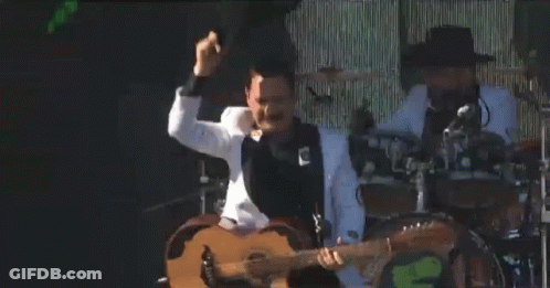 A Man In A White Tuxedo Is Playing A Guitar On Stage GIF