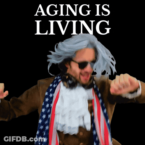 A Man In A Wig And Scarf Is Dancing In Front Of A Sign That Says Aging Is Living GIF