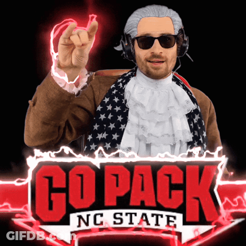A Man In A Wig And Sunglasses Stands In Front Of A Go Pack Nc State Sign GIF
