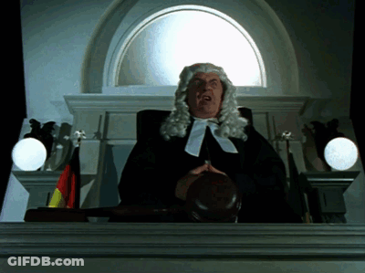 A Man In A Wig Is Holding A Judge 'S Gavel In Front Of A Window GIF