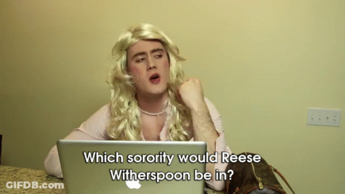 A Man In A Wig Is Sitting In Front Of An Apple Laptop And Asking Which Sorority Would Reese Witherspoon GIF