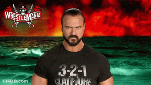 A Man In A Wrestlemania Shirt Stands In Front Of A Ocean GIF