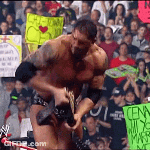 A Man In A Wrestling Match Is Holding A Sign That Says ' Cena ' On It . GIF