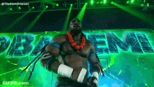 A Man In A Wrestling Outfit Is Standing In Front Of A Green Sign That Says " Baem " GIF