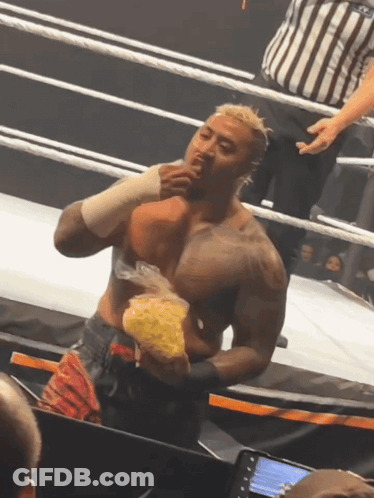 A Man In A Wrestling Ring Holds A Bag Of Chips In His Hand GIF