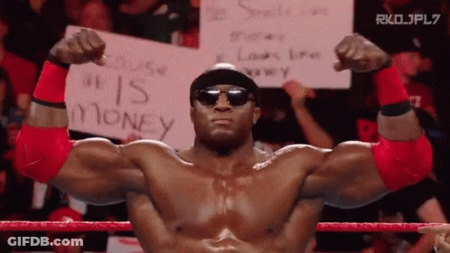 A Man In A Wrestling Ring Holds A Sign That Says " He Is Money " GIF