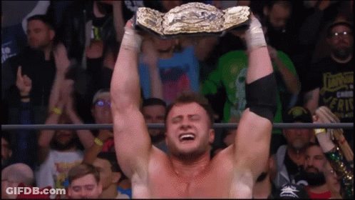 A Man In A Wrestling Ring Is Holding A Championship Belt Above His Head GIF