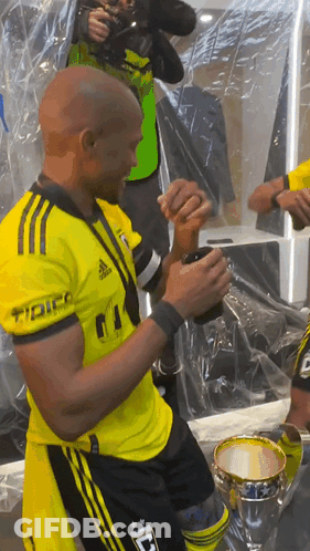 A Man In A Yellow Adidas Shirt Holds A Cup In His Hand GIF