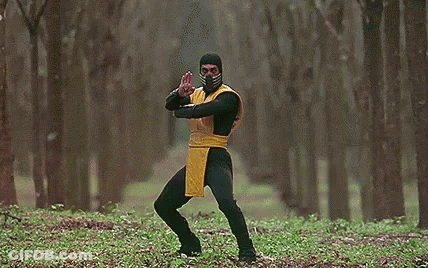 A Man In A Yellow And Black Costume Is Standing In The Woods Holding A Long Sword . GIF