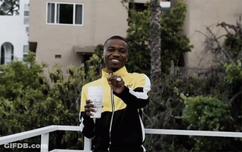A Man In A Yellow And Black Jacket Is Holding A Cup That Says ' Almost Naked ' On It GIF