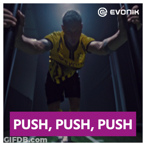 A Man In A Yellow And Black Jersey Stands In A Dark Room With A Sign That Says Push Push Push GIF
