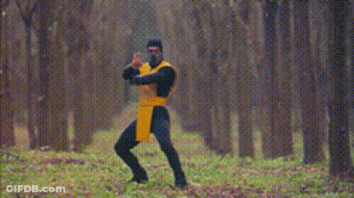 A Man In A Yellow And Black Outfit Is Standing In The Woods With The Words Get Over Here GIF
