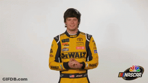 A Man In A Yellow And Black Racing Suit Is Standing In Front Of A Sign That Says What ? GIF
