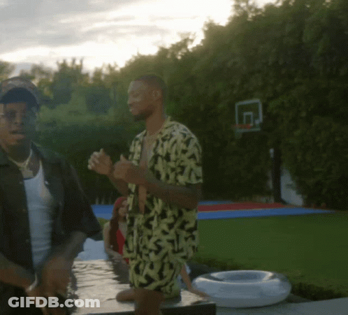 A Man In A Yellow And Black Shirt Stands Next To Another Man In A Black Shirt GIF