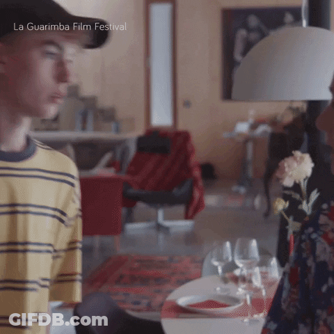A Man In A Yellow And Black Striped Shirt Is Standing In A Living Room With La Guarimba Film Festival Written On The Bot GIF