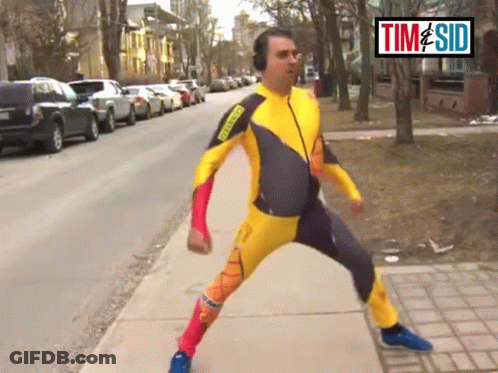 A Man In A Yellow And Black Suit Is Walking Down A Sidewalk In Front Of A Sign That Says Time Sid GIF