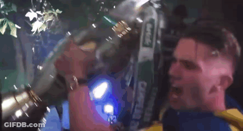 A Man In A Yellow And Blue Shirt Is Holding A Large Trophy In His Mouth GIF