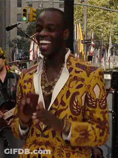 A Man In A Yellow And Purple Jacket Is Smiling And Holding A Cell Phone GIF
