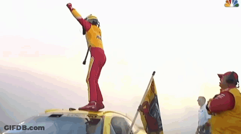 A Man In A Yellow And Red Racing Suit Is Dancing In Front Of A Crowd . GIF