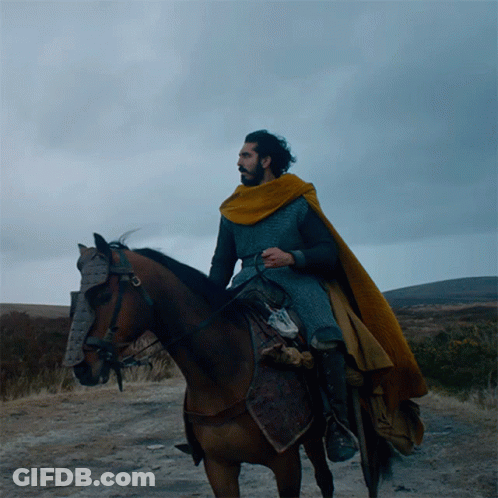 A Man In A Yellow Cape Is Riding A Horse On A Dirt Road GIF