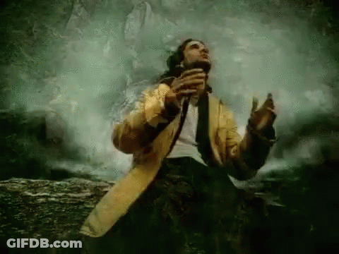 A Man In A Yellow Coat And Tie Is Singing Into A Microphone . GIF