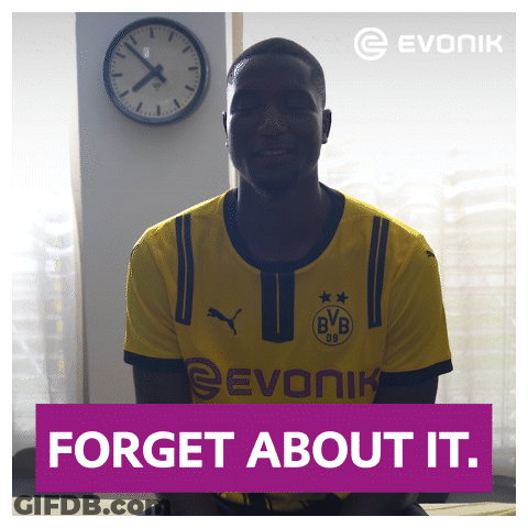A Man In A Yellow Evonik Shirt Is Smiling In Front Of A Clock GIF