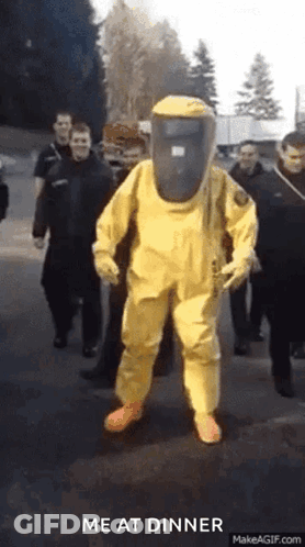 A Man In A Yellow Hazmat Suit Is Walking Down A Street GIF