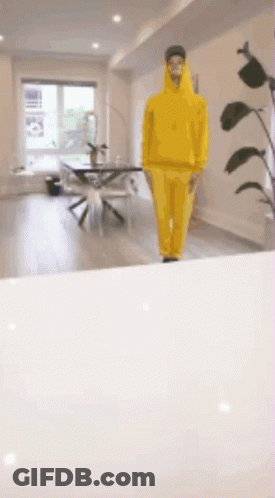 A Man In A Yellow Hoodie Is Walking In A Room GIF