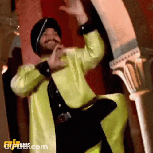 A Man In A Yellow Jacket And Black Hat Is Dancing In Front Of A Sign That Says Rajabets On It GIF