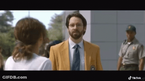 A Man In A Yellow Jacket And Tie Is Talking To A Woman While A Police Officer Stands Behind Him . GIF