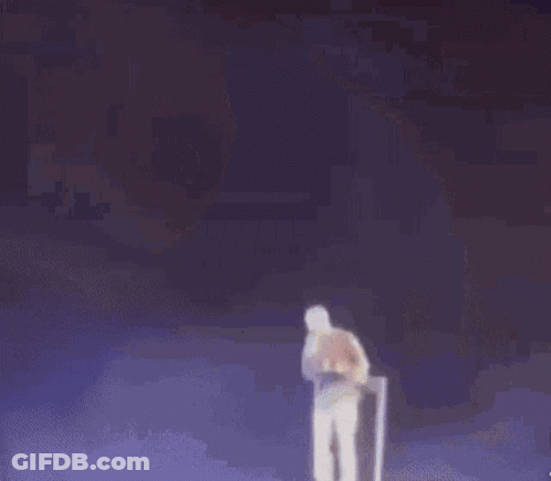 A Man In A Yellow Jacket And White Shorts Is Standing On A Stage . GIF