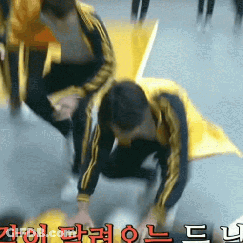A Man In A Yellow Jacket Is Kneeling Down In Front Of A Sign With Chinese Writing On It GIF
