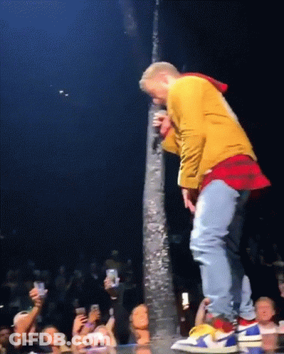 A Man In A Yellow Jacket Is Singing Into A Microphone While Standing On A Stage GIF