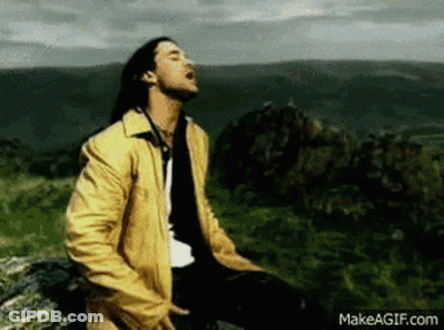 A Man In A Yellow Jacket Is Sitting On Top Of A Hill . GIF