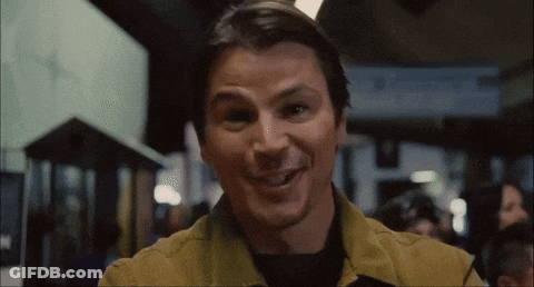 A Man In A Yellow Jacket Is Smiling In A Crowded Room GIF