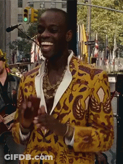 A Man In A Yellow Jacket Is Smiling In Front Of A Green Light GIF