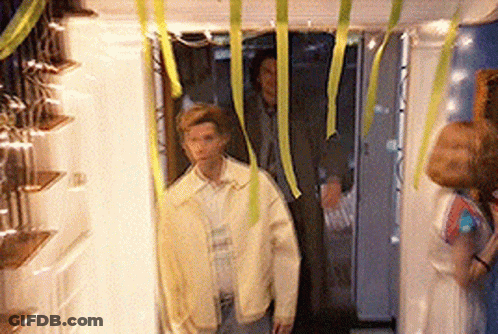 A Man In A Yellow Jacket Is Standing In A Hallway With Ribbons Hanging From The Ceiling GIF