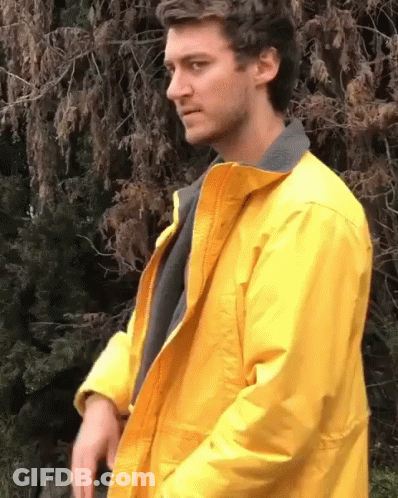 A Man In A Yellow Jacket Is Standing In Front Of A Tree GIF