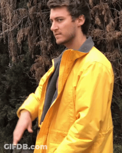 A Man In A Yellow Jacket Is Standing In Front Of Trees GIF