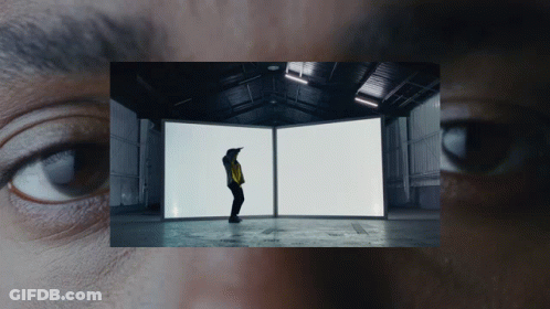 A Man In A Yellow Jacket Is Standing In Front Of Two White Boxes GIF