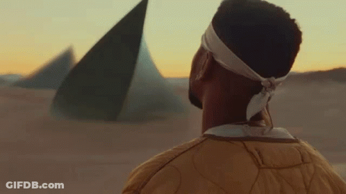 A Man In A Yellow Jacket Is Walking Through A Sandy Desert . GIF