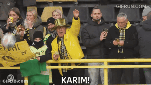 A Man In A Yellow Jacket Says Karim In Front Of A Group Of People GIF